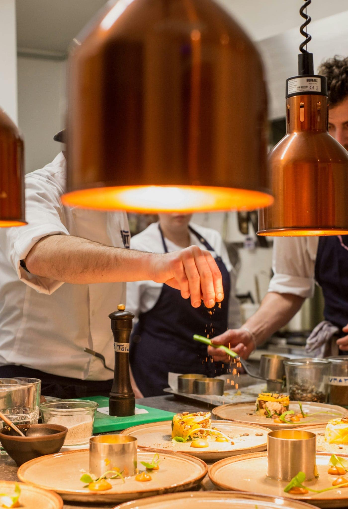 Chefs plating dishes under the warm copper lamps of a restaurant pass